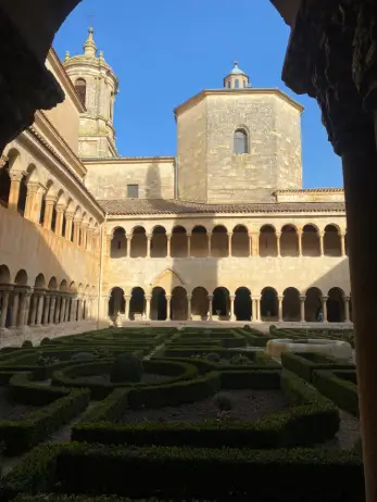 Detalle del claustro románico del monasterio de Santo Domingo de Silos, con su jardín geométrico y las torres de la iglesia al fondo.