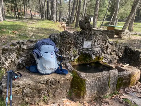 Mochila descansando junto a una fuente natural en el área recreativa de Pinarejos, un punto clave en la etapa hacia Santo Domingo