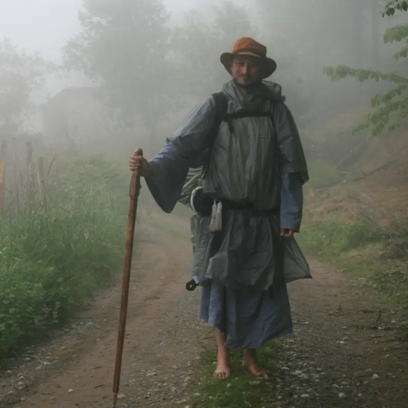 Peregrino vestido con túnica y descalzo en un sendero del Camino de Santiago, representando la tradición y la pureza del peregrinaje.