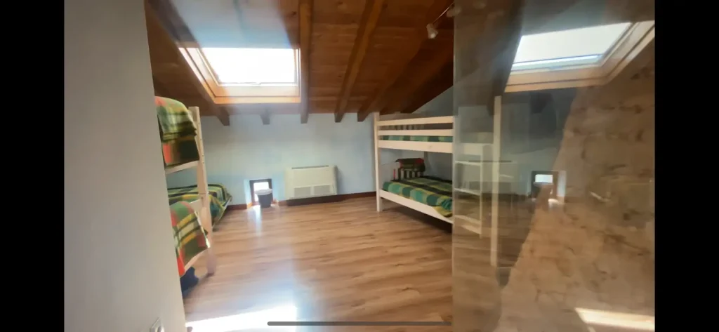 Habitación con literas en el Albergue La Corneja de Mecerreyes. Espacio acogedor con techo de madera y tragaluz para luz natural.