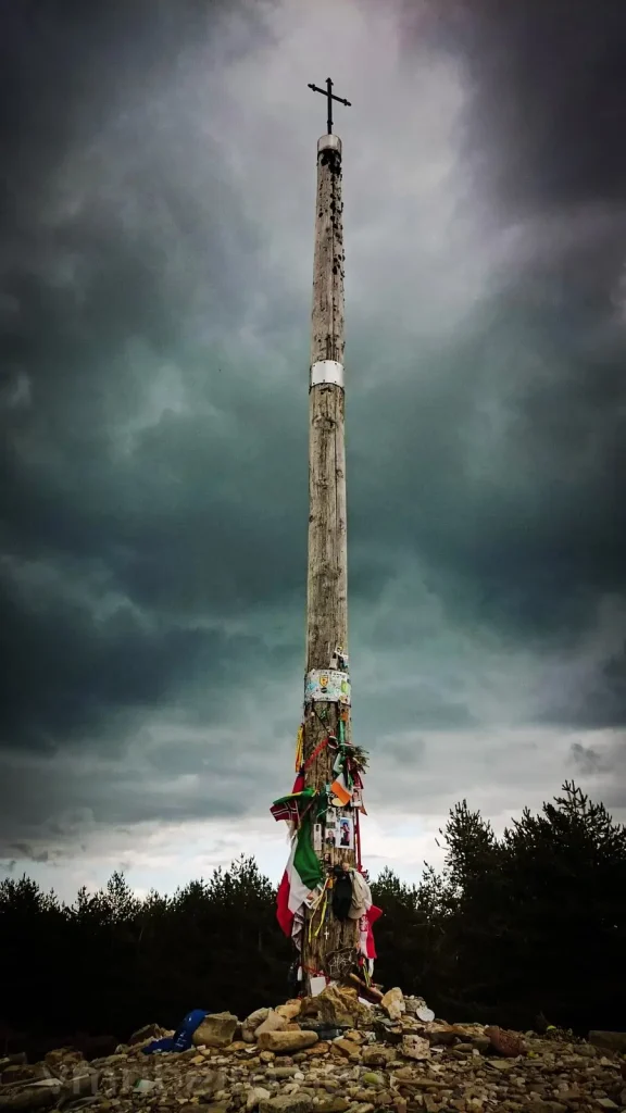 Cruz de Ferro en el Camino de Santiago rodeada de piedras dejadas por peregrinos, con cielo nublado y ambiente solemne