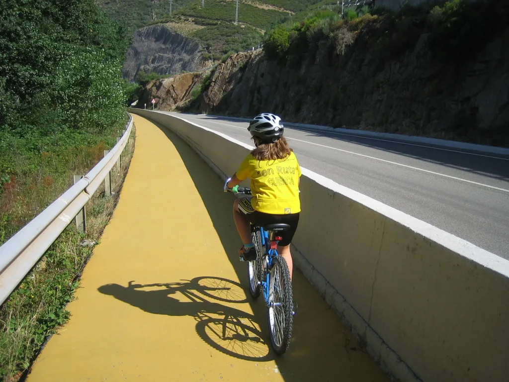 Niña con casco y camiseta amarilla pedaleando por un carril bici paralelo a la carretera en el Camino de Santiago.
