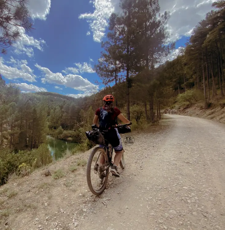 Mujer recorriendo en bicicleta eléctrica una etapa del Camino de Santiago por una pista forestal junto a un río
