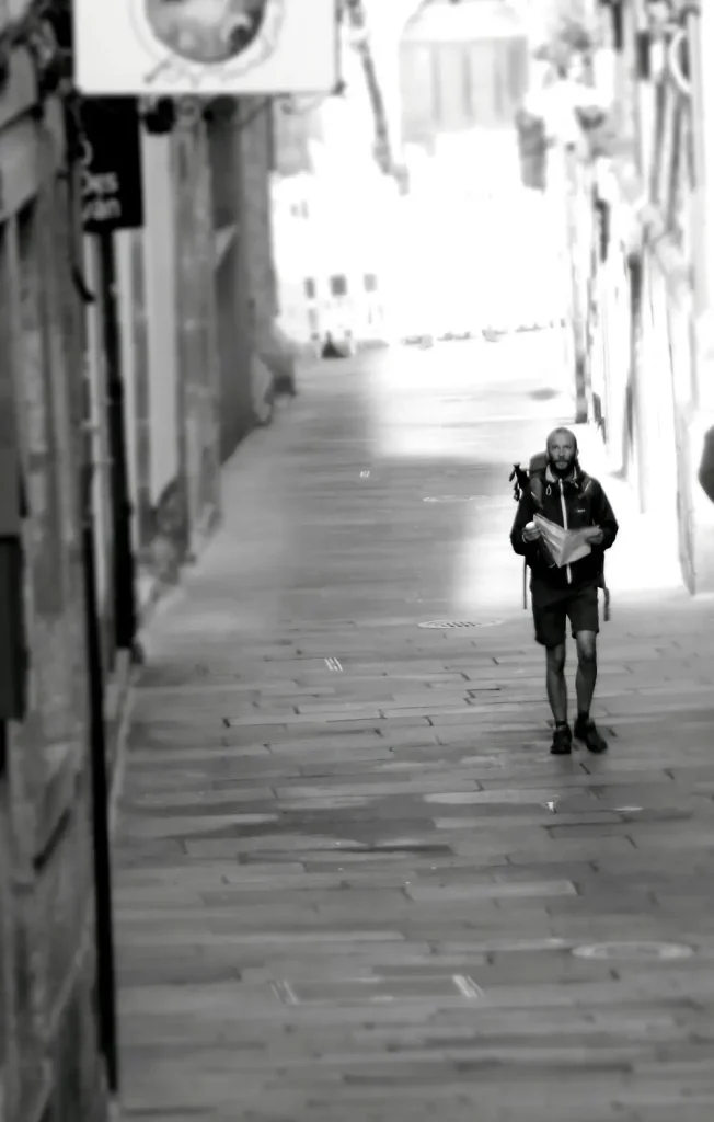 Peregrino solitario avanzando por una calle empedrada en Santiago de Compostela, con mochila al hombro y mapa en mano, símbolo de introspección y esfuerzo en el Camino de Santiago.