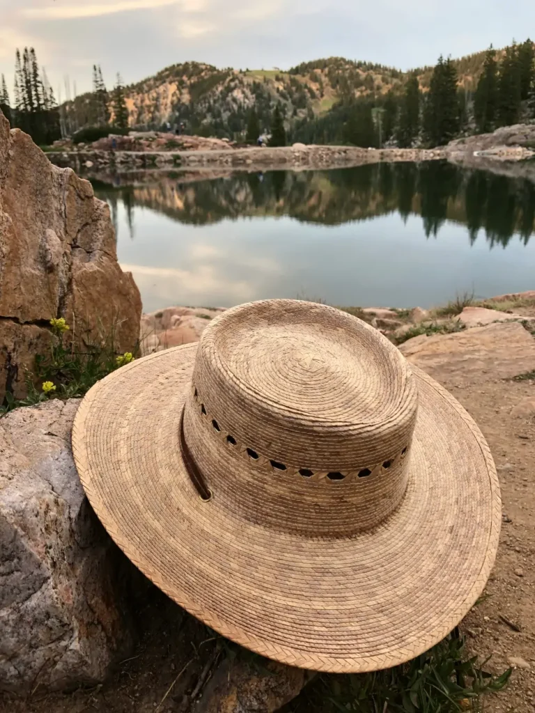 Sombrero de paja con ventilación colocado sobre una roca junto a un lago de montaña, ideal para etapas soleadas del Camino de Santiago