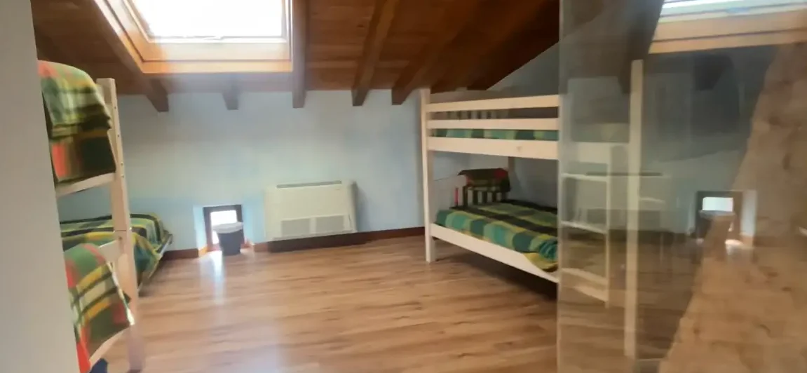 Habitación con literas en el Albergue La Corneja de Mecerreyes. Espacio acogedor con techo de madera y tragaluz para luz natural.