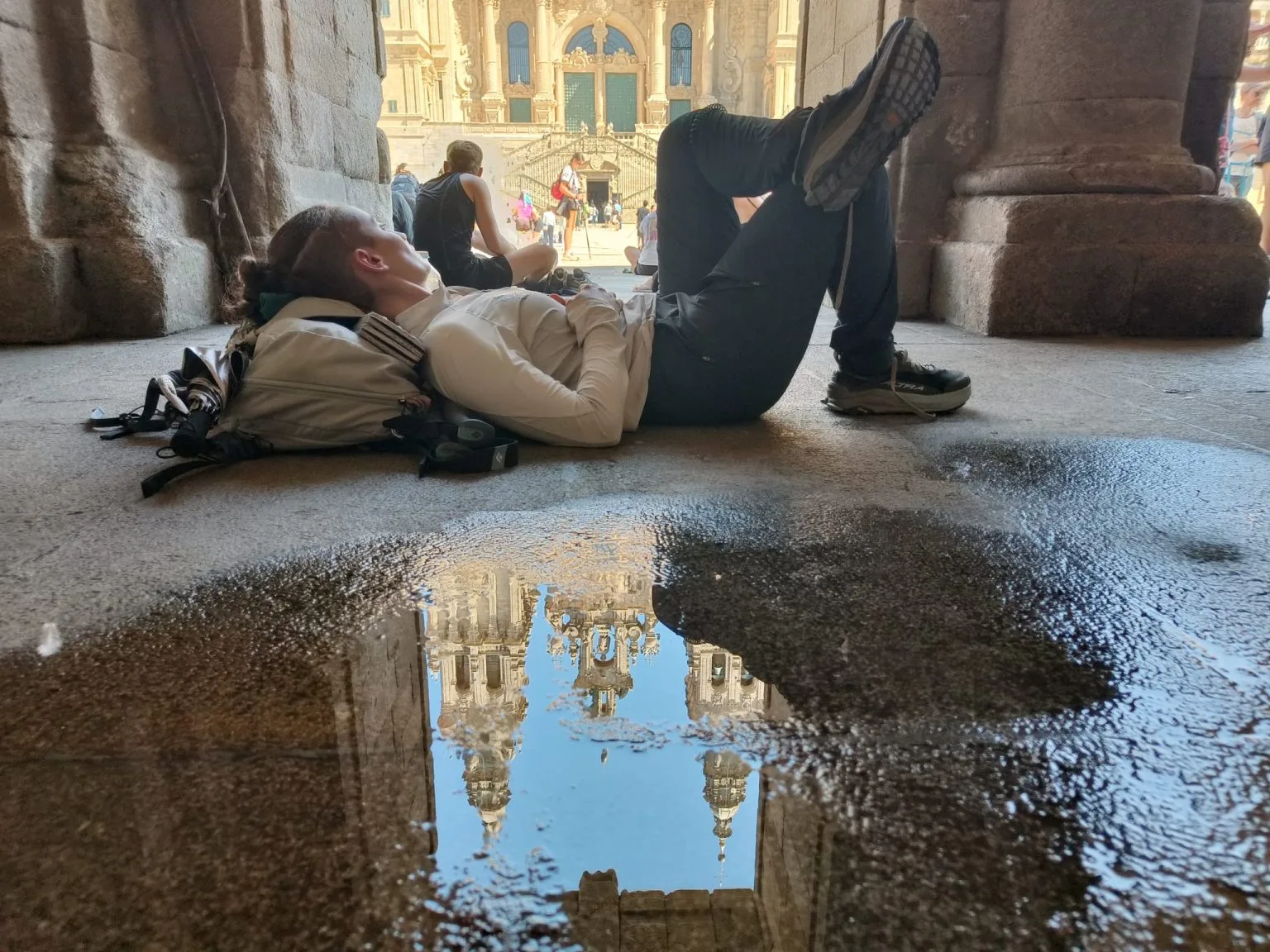 Peregrina descansando en la plaza del Obradoiro con la catedral de Santiago reflejada en un charco