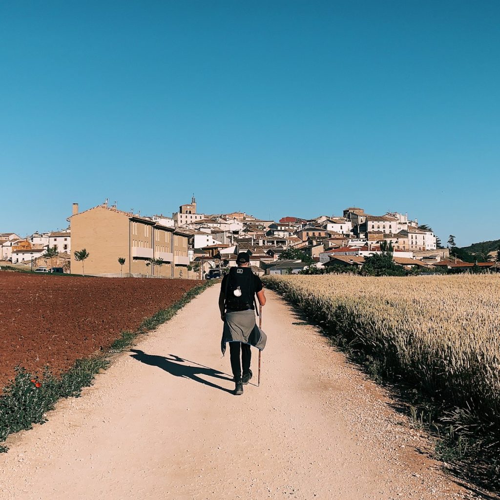 Persona caminando por un camino de tierra entre campos